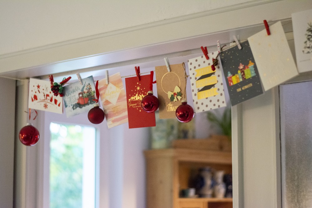 Weihnachtskarten und Kugeln an einer Girlande mit Wäscheklammern befestigt.