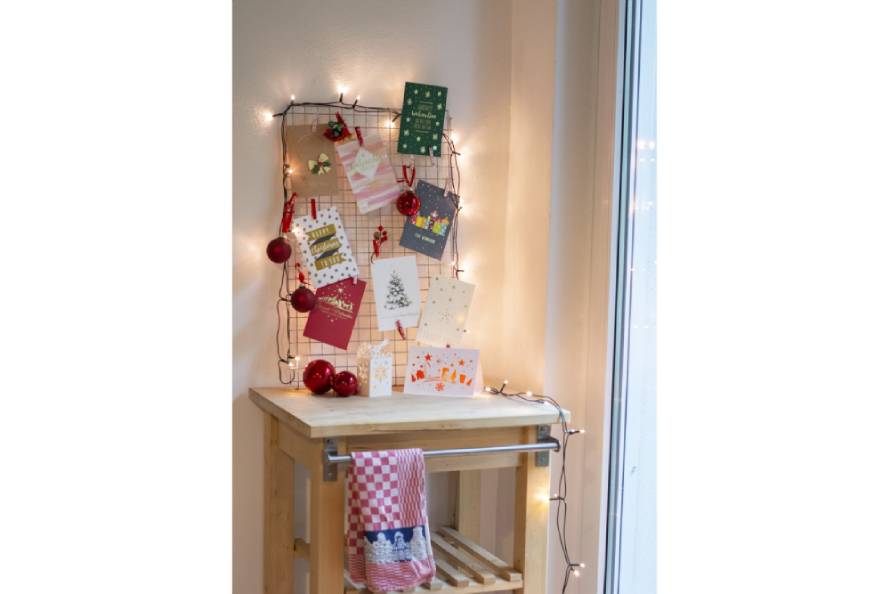 Weihnachtskarten an Gitter mit Lichterkette und rotem Weihnachtsschmuck