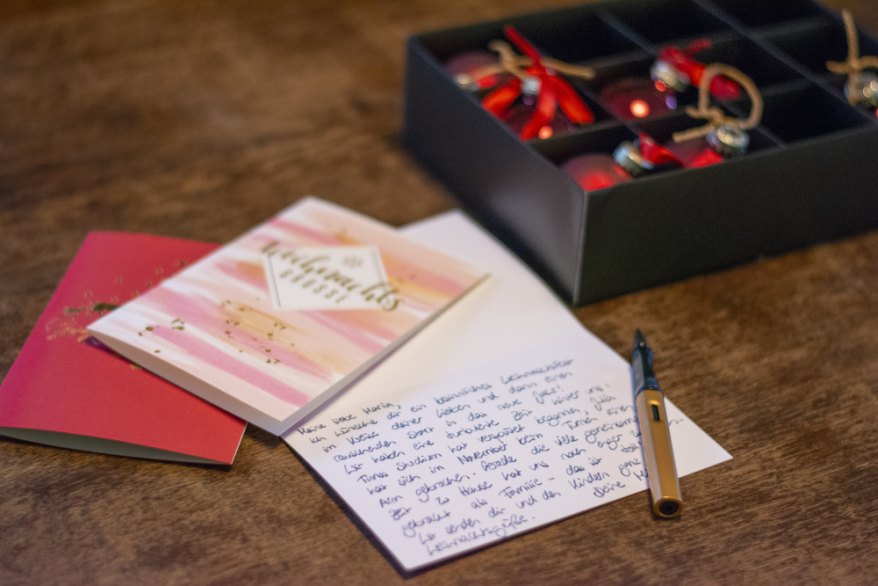Handgeschriebene Weihnachtskarte und einem Lamy-Füller neben Weihnachtskugeln auf einem isch