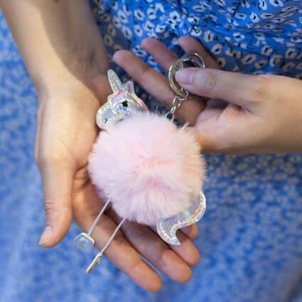 Ein Person mit einem blau, geblümten Kleid hält einen Glücksbringer gegen Prüfungsangst in der Hand. Es handelt sich um einen Schlüsselanhänger mit einem Einhornmotiv.