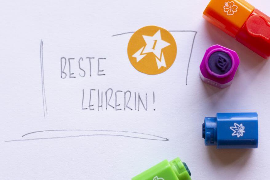 Auf ein Blatt Papier wurde "Beste Lehrerin" geschrieben und mit einem Sticker verziert. Darum verteilt liegen verschiedene Stempel von Brunnen.