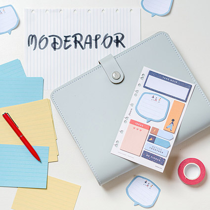 Auf einem weißen Untergrund liegt ein hellgrauer Leder-Planer von Filofax. Darunter ein Zettel ausgerissener, linierter Zettel mit dem Wort "Moderator". Drumherum sind verschiedene Materialien verteilt, die ein Moderator benötigt: Stift, Klebezettel, Karteikarten und Klebeband. Foto: Johanna Rundel