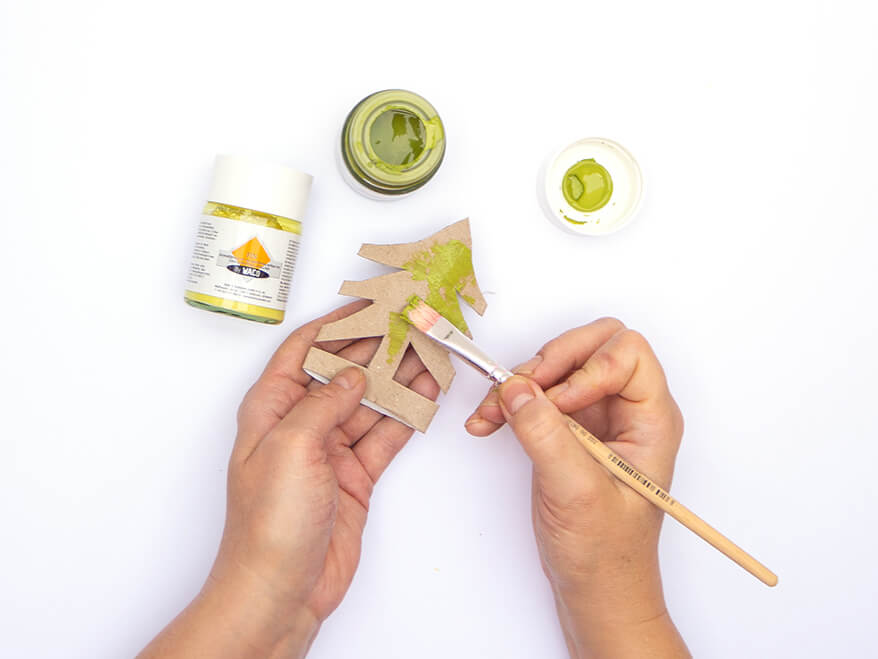 Jemand malt mit einem Pinsel grüne Farbe von Baier und Schneider auf einen, aus einer leeren Klopapierrolle ausgeschnittenen, Tannenbaum auf. Der Untergrund ist weiß. Foto: Johanna Rundel