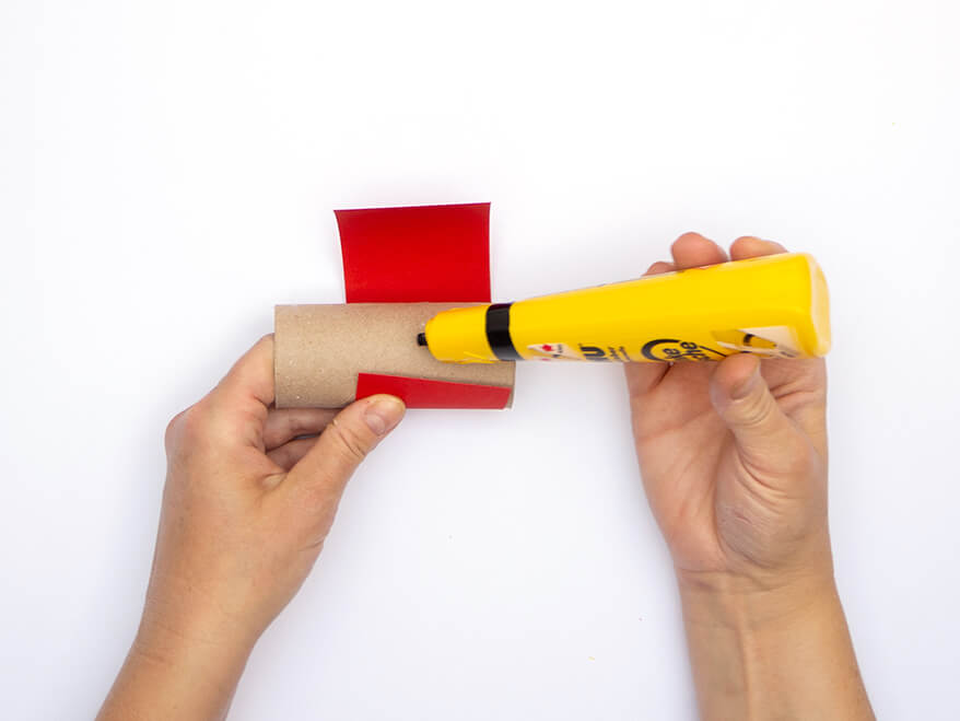 Jemand klebt einen Streifen rotes Tonpapier von Heyda auf eine leere Klopapierrolle. Der Untergrund ist weiß. Foto: Johanna Rundel