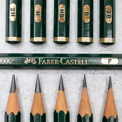 In der oberen Reihe sieht man nebeneinander die Enden von fünf dunkelgrünen Bleistiften. Sie haben einen goldenen Ring. Auf einer ebenfalls goldenen Fläche sieht man die Bleistiftstärke. In der unteren Reihe sieht man die Bleistiftspitzen. Dazwischen liegt ein Bleistift quer. Auf diesem ist Faber Castell zu lesen. Foto: Johanna Rundel