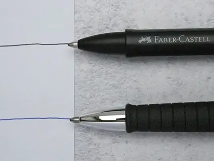 Zwei schwarze Kugelschreiber von Faber-Castell liegen waagerecht übereinander angeordnet auf einem hellgrauen Untergrund. Die Kugelschreiberspitzen zeigen auf ein weißes Blatt Papier, auf dem ein schwarzer und ein blauer Kugelschreiberstrich zu den Spitzen hinführen. Foto: Johanna Rundel
