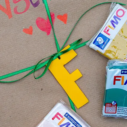 Ein, aus Fimo von Staedtler, gebastelter Geschenkanhänger ist mit einem grünen Band auf einem mit Packpapier verpackten Geschenk gebunden.