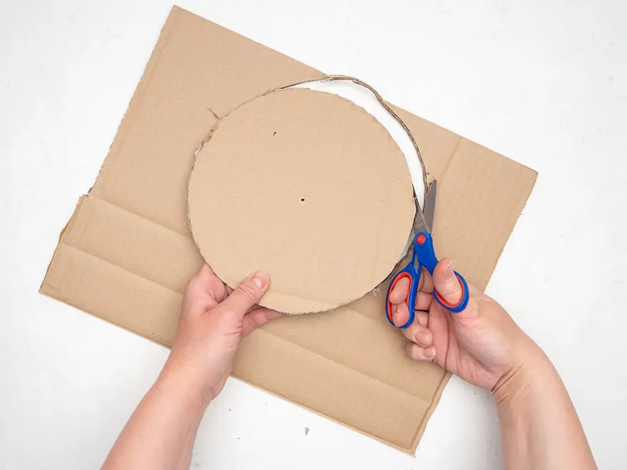 Jemand schneidet mit einer Schere von Staedtler aus einem Stück Pappe einen Kreis aus.