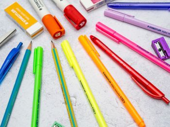 Verschiedene Stifte, Spitzer, Radiergummis und Marker von STAEDTLER liegen farbig sortiert auf einer grauen Unterlage. Foto: Johanna Rundel