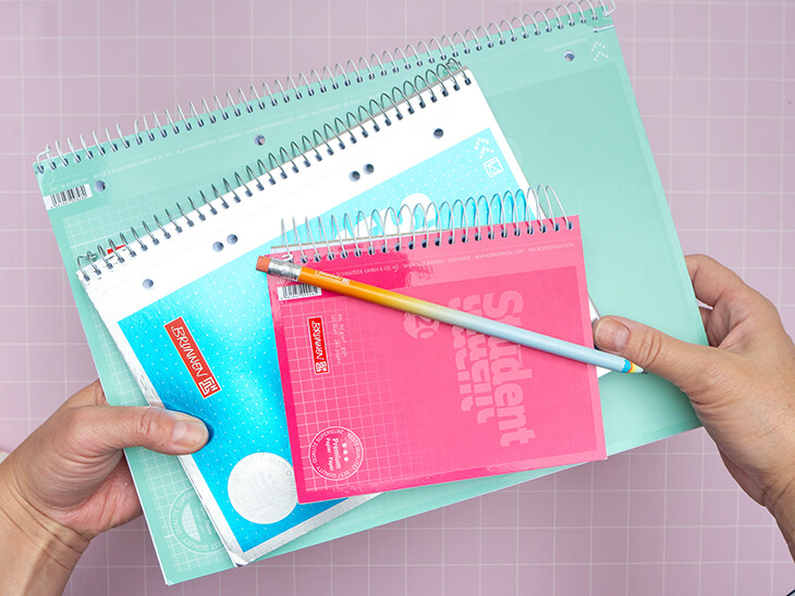 Jemand hält drei aufeinandergestapelte Collegeblöcke in verschiedenen Formaten von Brunnen in die Kamera. A4 liegt unten, darauf A5 und obendrauf A6. Foto: Johanna Rundel