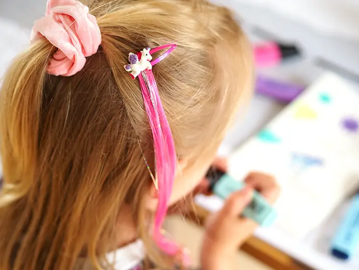Ein Mädchen hat eine Einhorn-Klammer mit einer künstlichen, pinken Strähne von Coppenrath im blonden Haar. Foto: Johanna Rundel