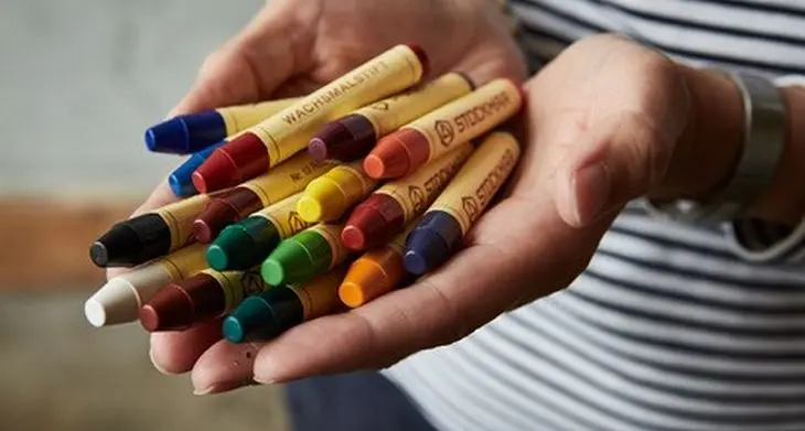 Eine Frau hält in ihren offenen Händen viele bunte Wachsmalstifte von STOCKMAR