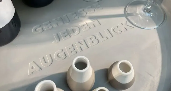 Mehrere Vasen stehen auf einem Teller, in den die Worte „Genieße jeden Augenblick“ eingraviert sind