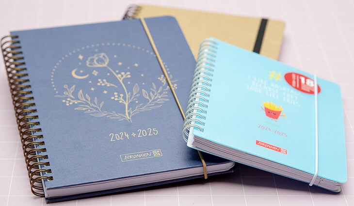 Drei verschiedenen Schülerkalender von BRUNNEN liegen nebeneinander auf einer rosa Unterlage. Foto: Johanna Rundel