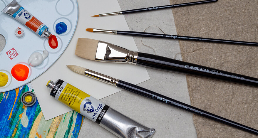 Auf einem grauen Untergrund liegen ein weißes Papier, ein Leinentuch und ein bemaltes Papier. Darauf liegen verschiedene Pinsel von Royal Talens und eine Farbtube. In der linken, oberen Ecke liegt eine Malpalette mit unterschiedlichen Farben in den Mulden. Foto: Johanna Rundel