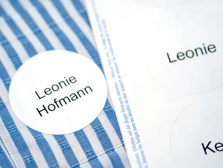 Auf einer blau-weiß-gestreiften Bluse liegt ein Bogen mit selbstklebenden Namensetiketten von Avery Zweckform. Foto: Johanna Rundel