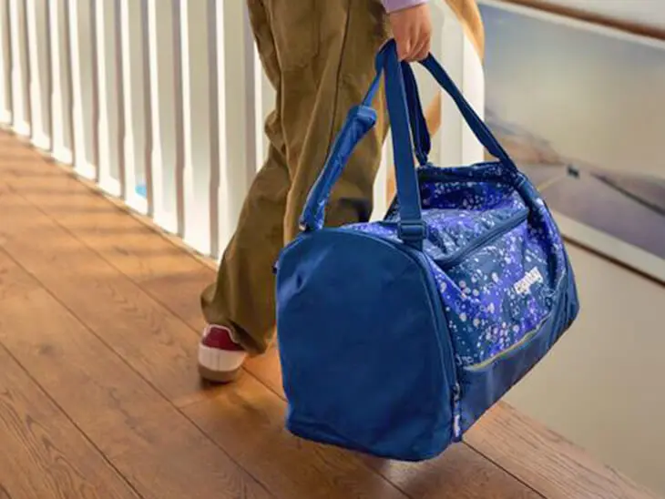 Ein Kind trägt eine große, blaue Sporttasche von ergobag zur Treppe.