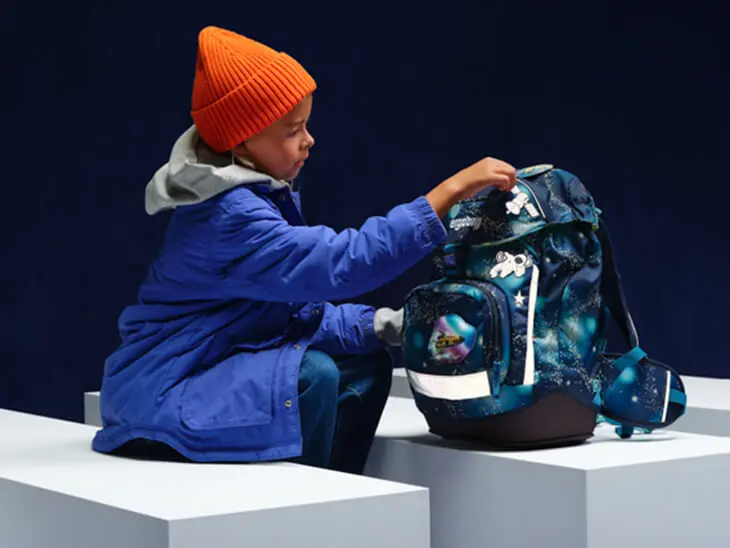 Ein Kind befestigt einen reflektierenden Klettie an seinem Schulranzen von ergobag.