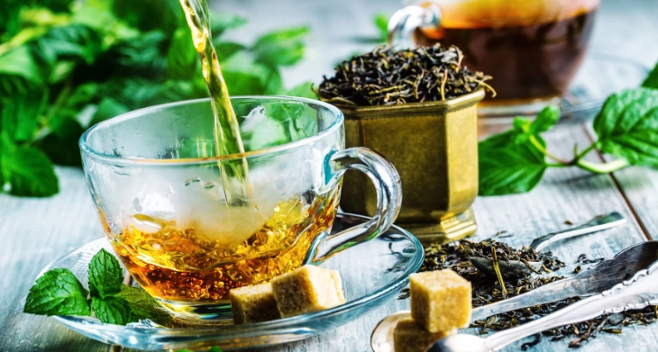 Frisch gebrühter Tee in Glastasse mit Zuckerwürfeln und Teeblättern