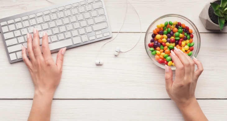 Hand greift zu Süßigkeiten neben Tastatur.