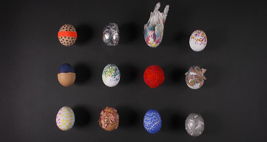 Auf einem schwarzen Untergrund liegen in 3 Reihen jeweils 4 unterschiedlich verzierte Ostereier. MAnche sind mit rotem Garn umwickelt, 2 sind mit Spitzer-Resten beklebt, andere sind mit Mustern bunt bemalt.
