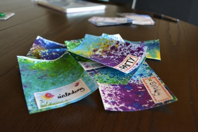 Auf einem Tisch liegen mit Wachsmalstiften bunt gestaltete Einladungen.