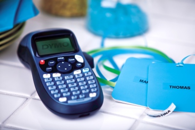 Ein Dymo LetraTag Beschriftungsgerät liegt auf einer Küchenbalage. Daneben liegen 2 mit Namen beschriftete Anhänger. 