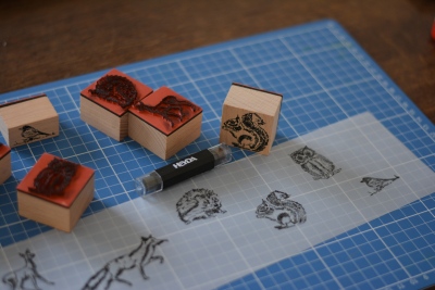 Auf einer Schneidematte liegen mehrere Stempel mit herbtlichen Motiven. Diese sind auf ein Transparentpapier gestempelt.