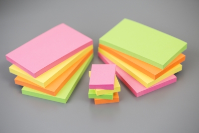 3 Stapel Klebezettel in bunten Farben liegen auf einem Tisch.
