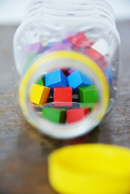 Nahaufnahme in eine geöffnete kleine Plastikflasche, welche mit bunten kleinen Holzklötzen gefüllt ist.