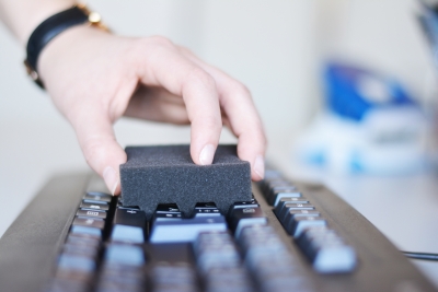 Jemand desinfiziert eine Tastatur mit einem Tastaturschwamm.