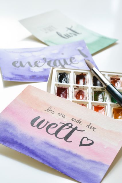 Flatlay zeigt 3 mit Aquarellfarben gestaltete Karten, auf die Brush-Lettering-Schriftzüge geletteret wurden.