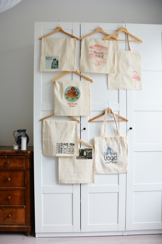 Verschiedene Designs von Jutebeuteln hängen an einem Schrank.