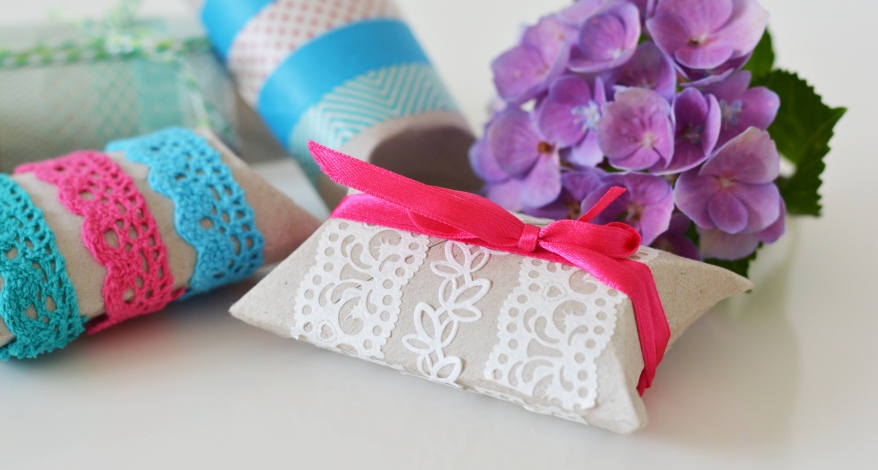 Mehrere Geschenkboxen aus Klopapierrollen, die mit Bändern verziert wurden. Im Hintergrund ist eine Blume zu sehen.