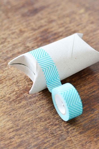 Eine zu einer Geschenkbox geknickte Klopapierrolle wird mit türkisem Washitape beklebt.