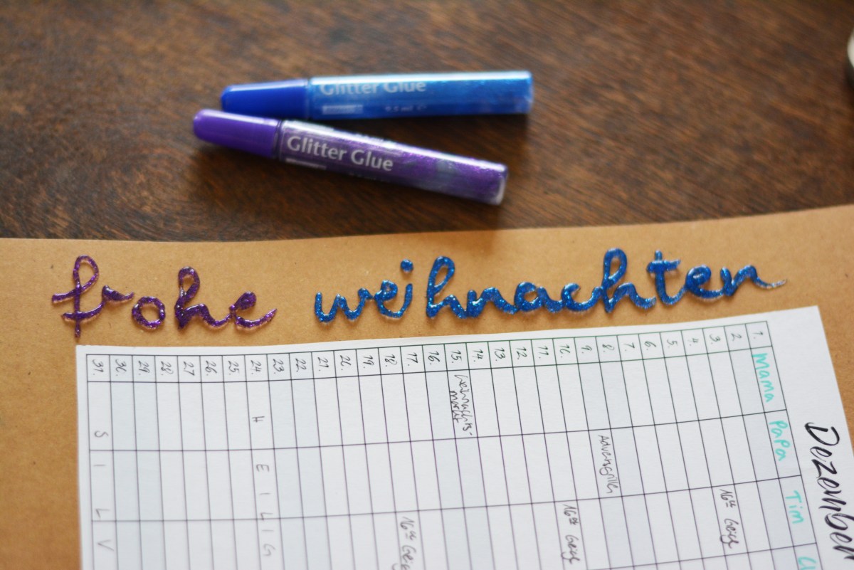 „Frohe Weihnachten“ mit Glitzerklebestift auf Planer auf braunem Karton.