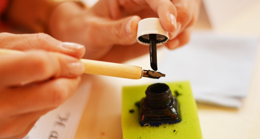 Eine Schreibfeder wird mit Tinte beträufelt.