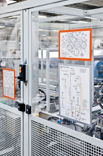 Anleitungsposter in farbigen Rahmen an Glastür einer Industrieanlage befestigt.