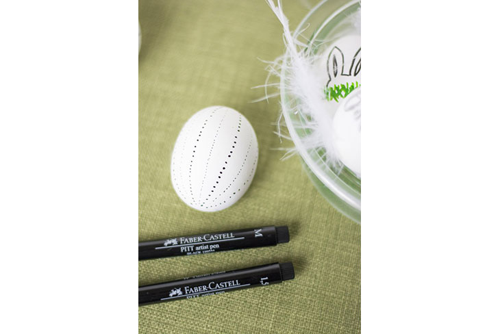 Ei mit schwarzem Punktmuster neben zwei schwarzen Faber-Castell-Stiften