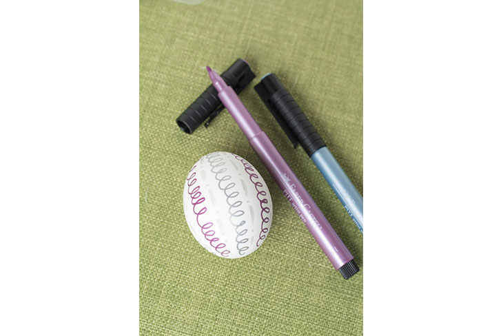 Ei mit Spiralmuster in Lila und Grau neben Brushpens