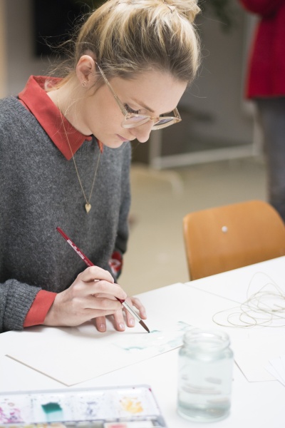 Sue von May & Berry sitzt am Tisch und malt mit Pinsel