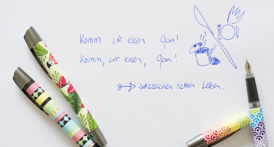 Drei bunte Füller der Marke Online liegen auf einem weißen Blatt Papier, welches mit Tinte beschriftet wurde. Ein Füller liegt mit geöffneter Kappe am rechten Bildrand.