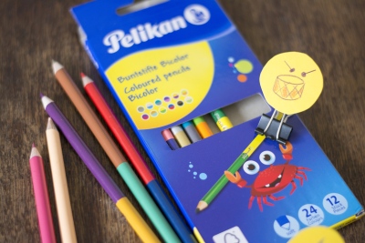 Einzelne Bicolor Buntstifte der Marke Pelikan liegen auf einem Tisch, die Verpackung der Schachtel liegt auch auf dem Tisch.