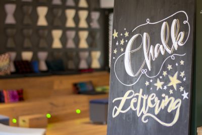 Geletterter Schriftzug „Chalk Lettering“ auf schwarzer Tafel mit Sternen.