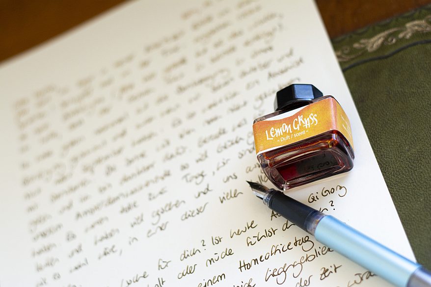 Flasche „Lemongrass“-Dufttinte neben Füller auf beschriebenem Blatt.