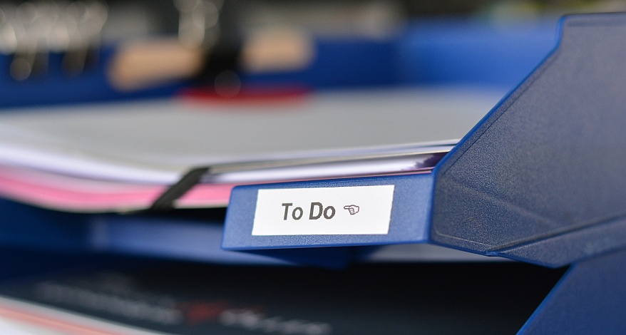 Blaue Ablage mit „To Do“-Etikett und Papierstapel im Büro.