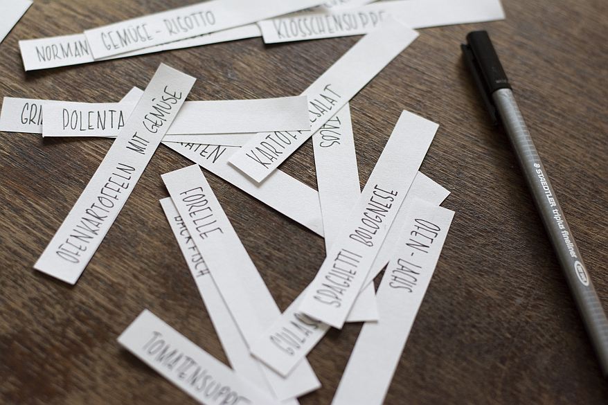 Essensvorschläge auf Papierstreifen, ausgebreitet neben einem schwarzen Fineliner