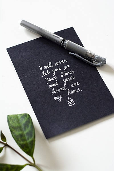 Handgeschriebener Spruch in Weiß auf schwarzer Karte mit Gelroller und Pflanze.