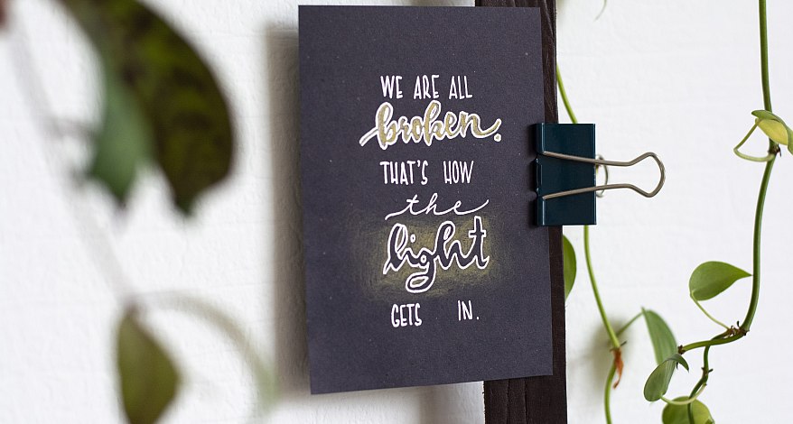 Schwarze Karte mit Lettering-Spruch, befestigt mit Klammer, umgeben von Pflanzen.