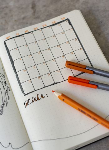 Notizbuch-Seite mit einem Monthly, darauf liegen diverse orange Stifte.